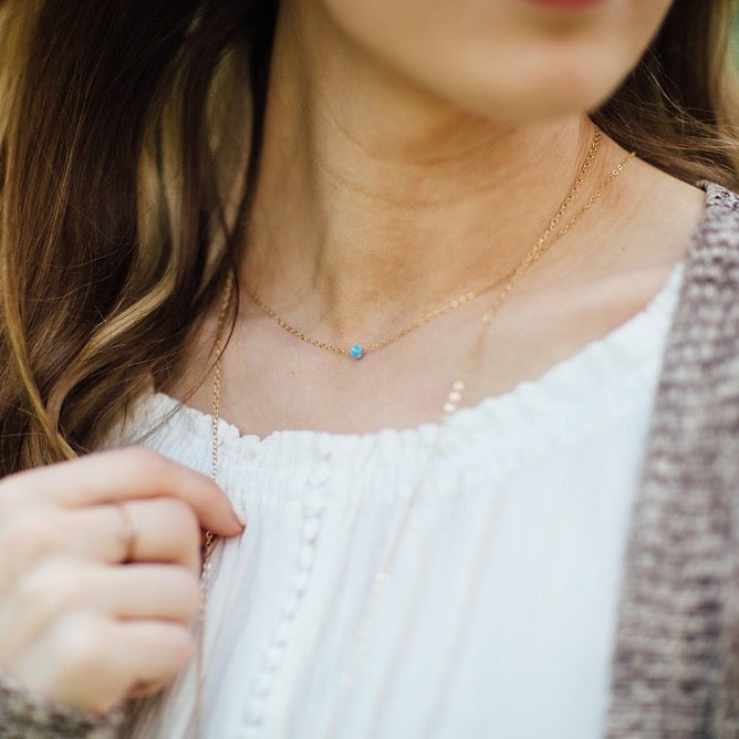 Close-up of a person wearing a delicate gold necklace with a small blue gemstone.